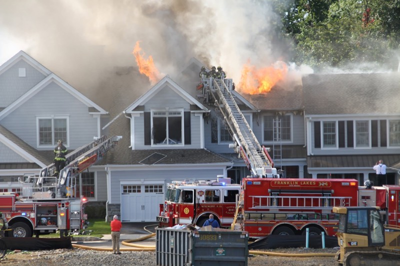 Flames through the roof of a large house as firefighters work from an aerial ladder above two fire engines