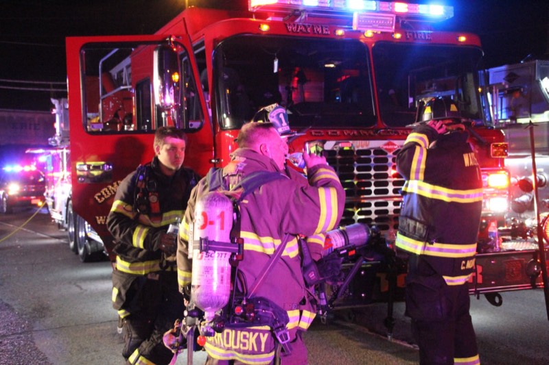 Firefighters wearing breathing apparatus in front of an engine with its emergency lights on