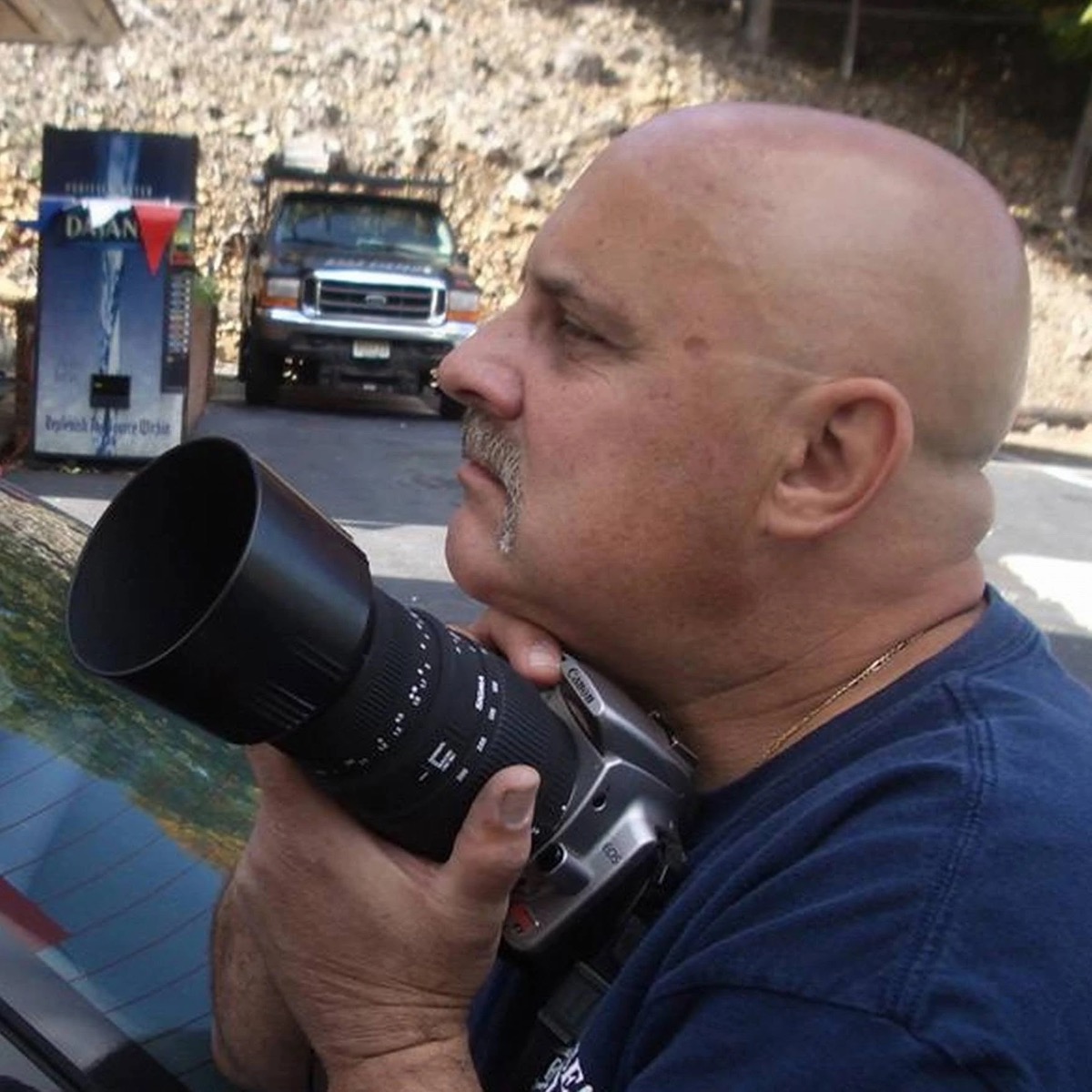 Ron Johnson in profile, steadying his Canon camera with a long telephoto lens