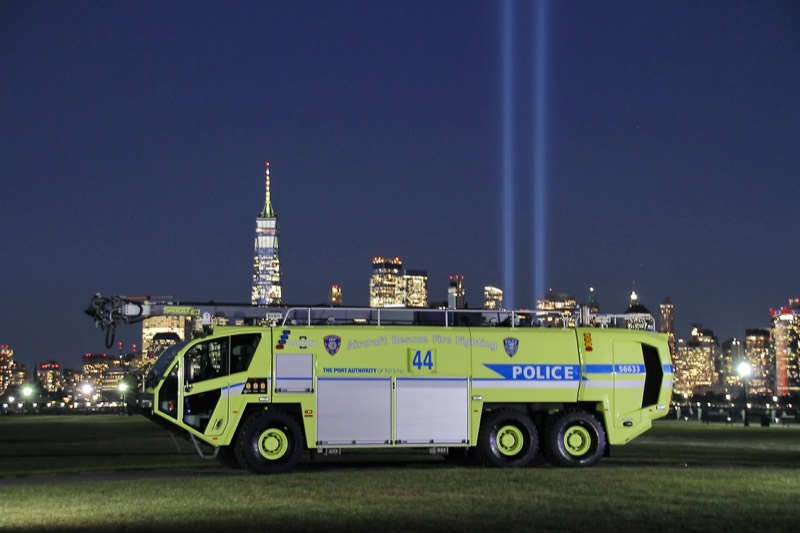 A lime-green Newark Liberty airport fire rescue truck on the lawn at night, the Tribute in Light beams behind it